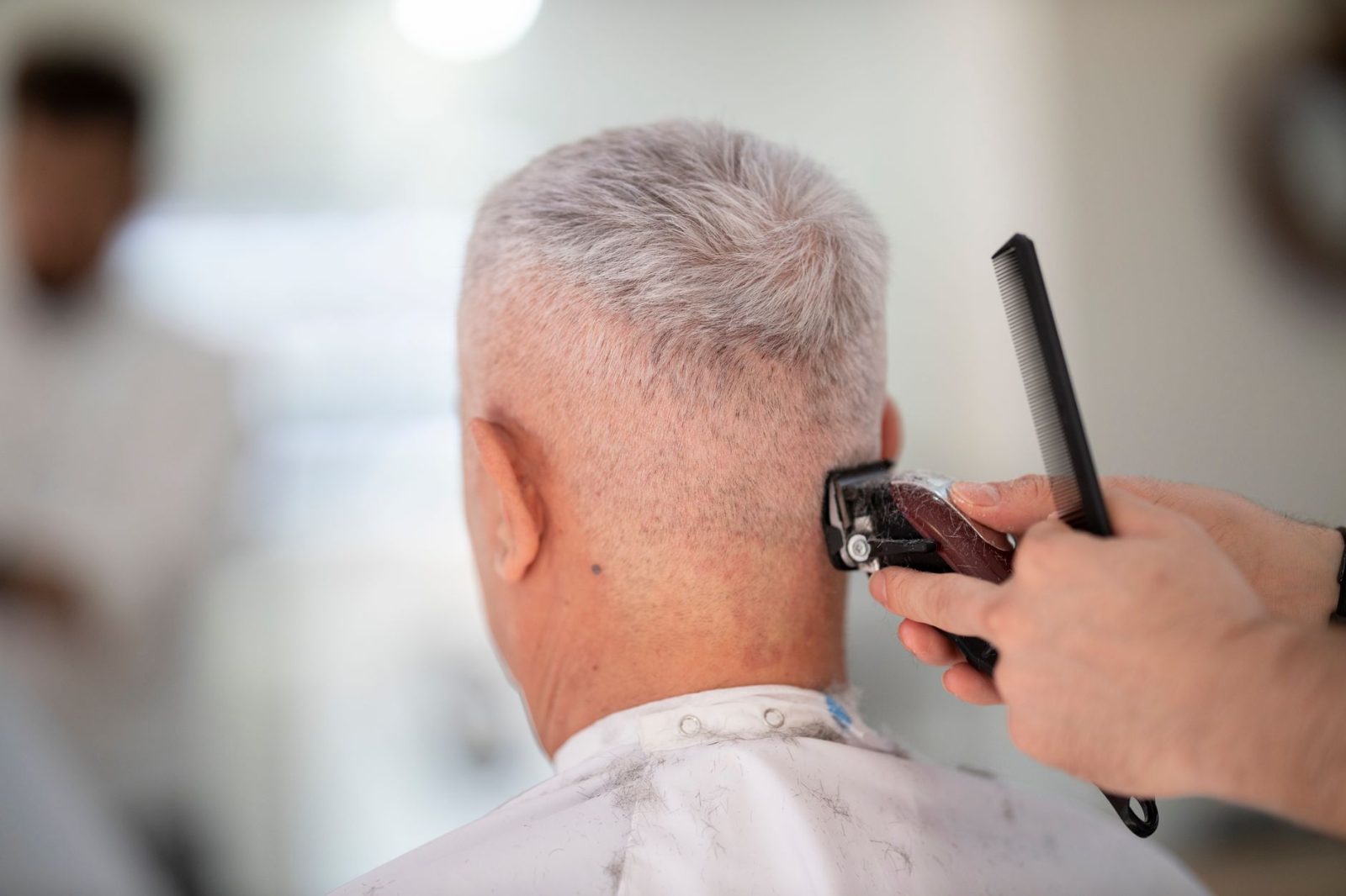 An elderly man having his hair trimmed by a barber using a clipper and comb